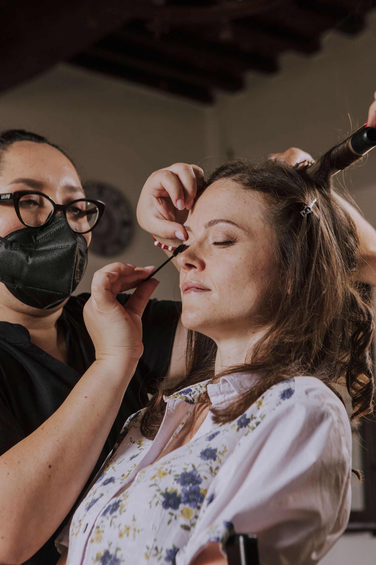 Stylist wearing protective mask works on wedding day hair preparation.