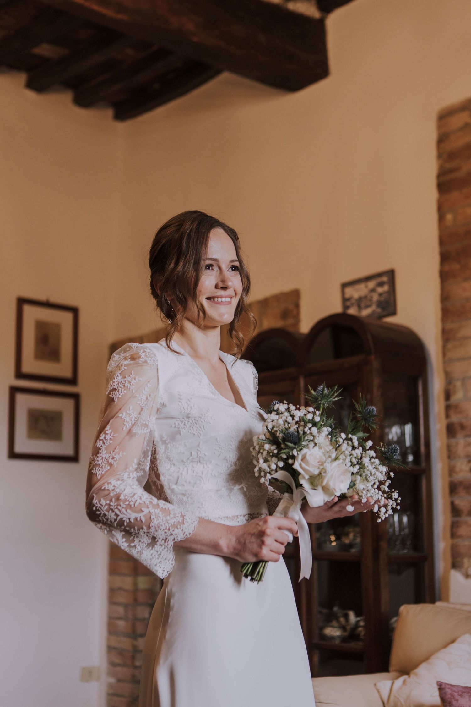 White lace wedding dress and bridal bouquet captured in rustic indoor setting.