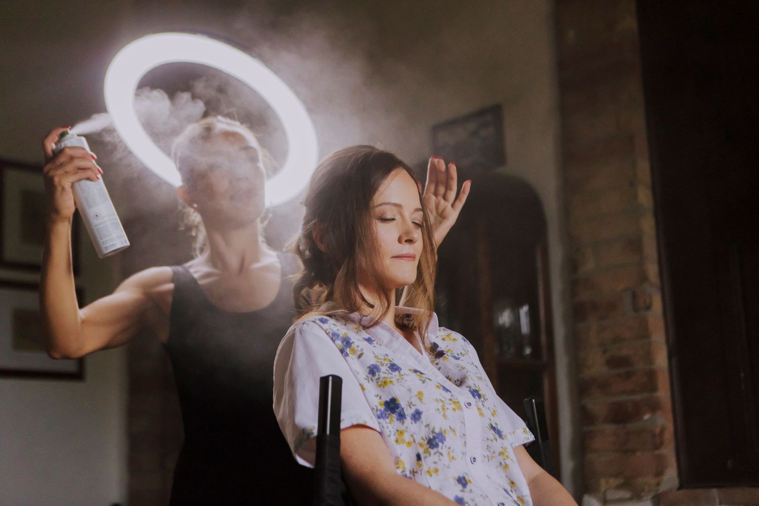 Hair styling session with dramatic ring light creating artistic glow in rustic setting.