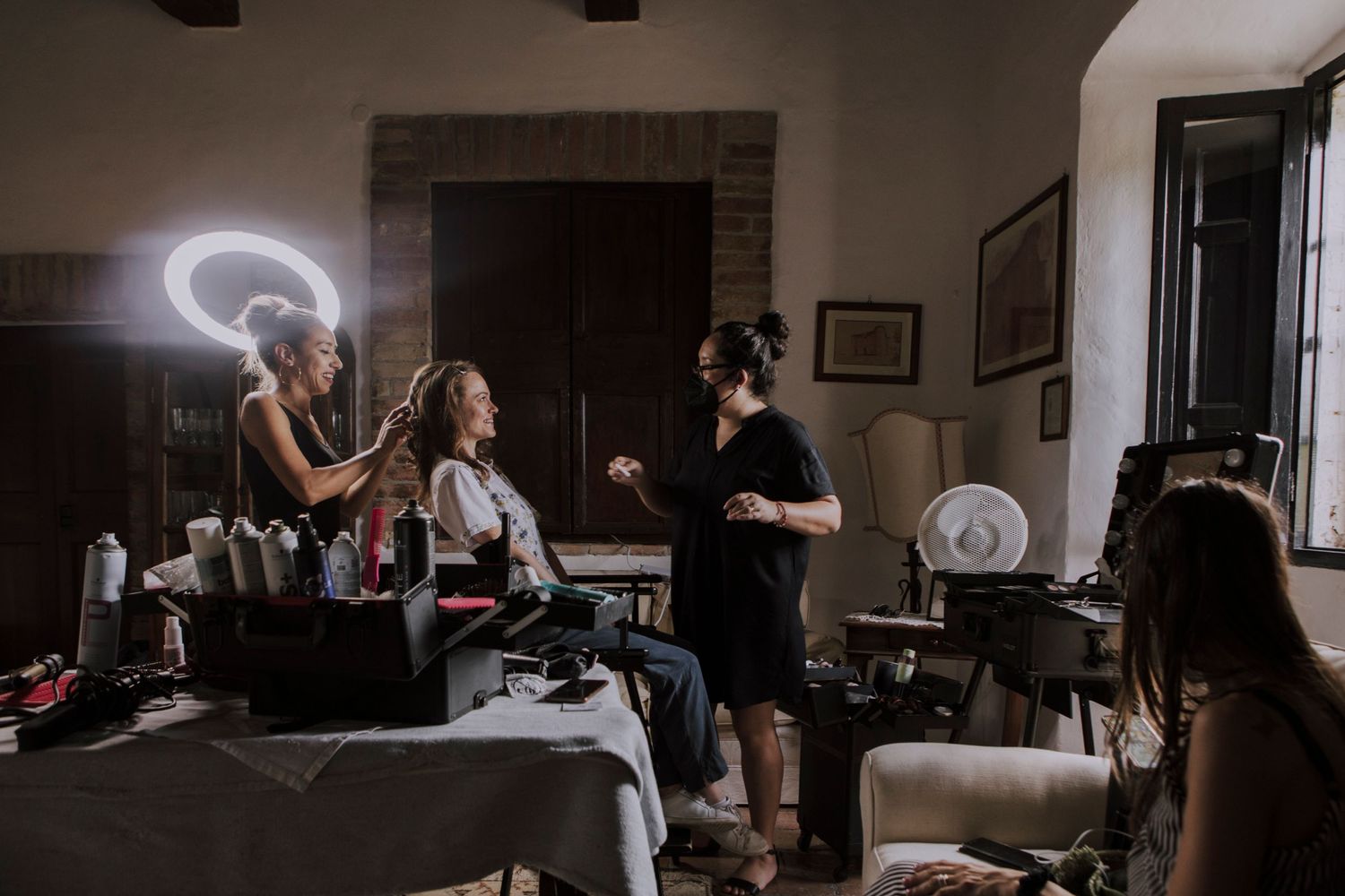 Wedding preparation scene in a rustic room with stylists using ring lights.