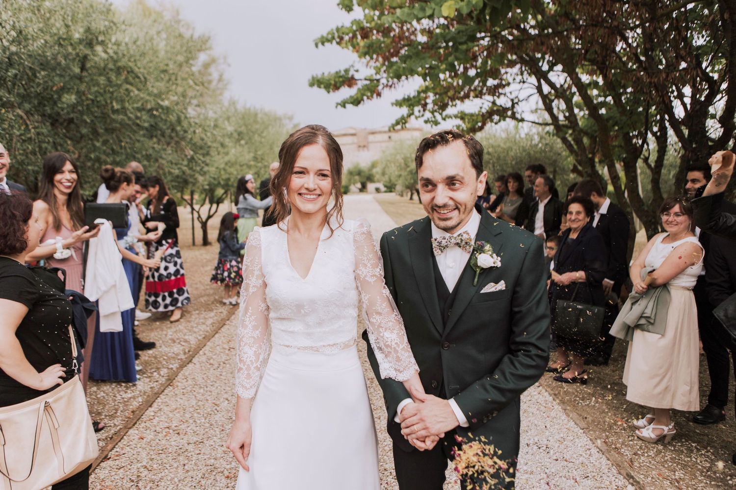 Couple laughs while walking down path lined with wedding guests during outdoor ceremony.