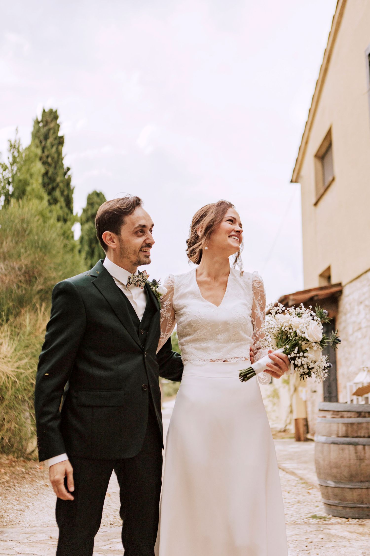 Elegant couple in formal wedding attire stands together on rustic outdoor path.