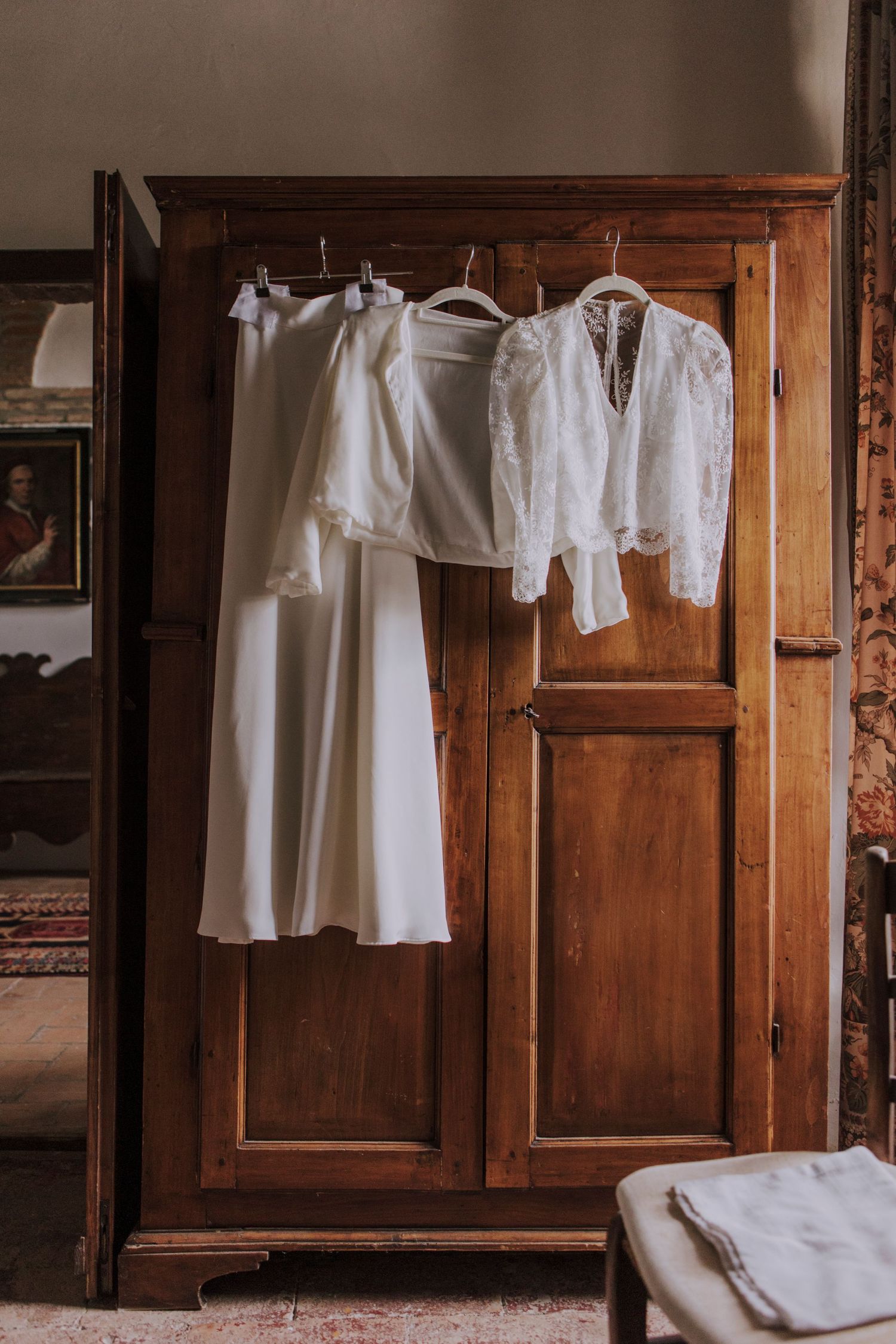 White wedding dress and lace top hanging on wooden vintage wardrobe.