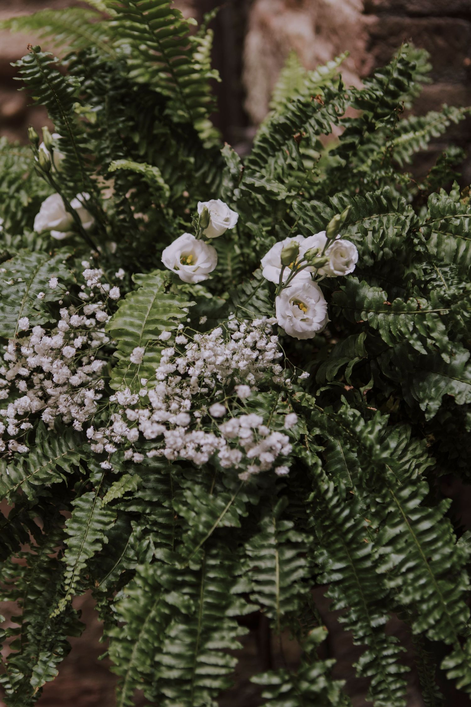 Delicate white flowers and ferns create an elegant wedding bouquet arrangement in moody lighting.