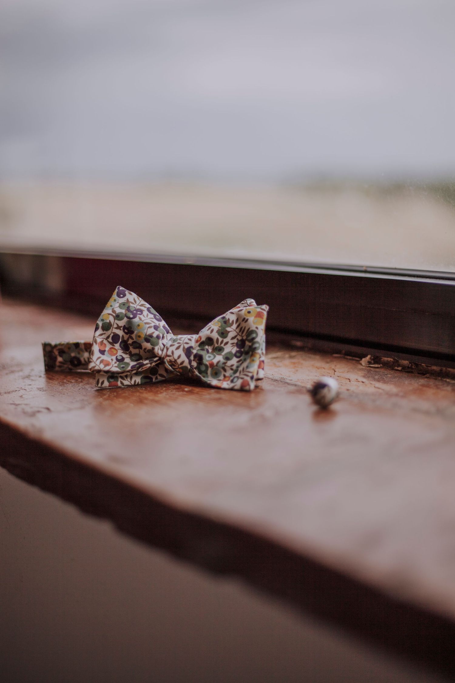 Floral patterned bow tie rests on wooden windowsill in moody lighting.