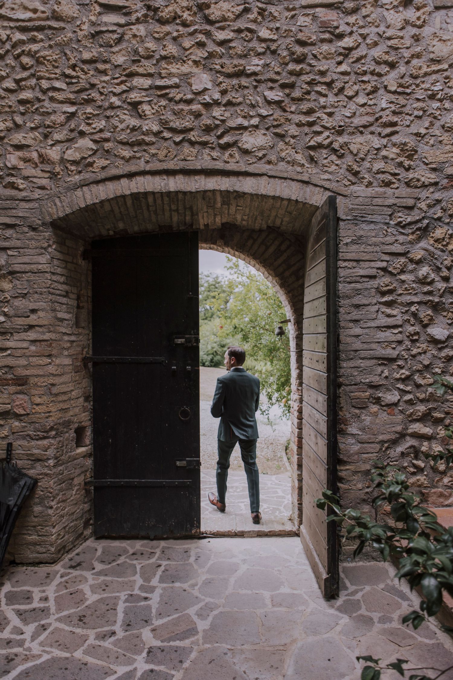 Stone archway with wooden door frame leads to a sunlit garden path.
