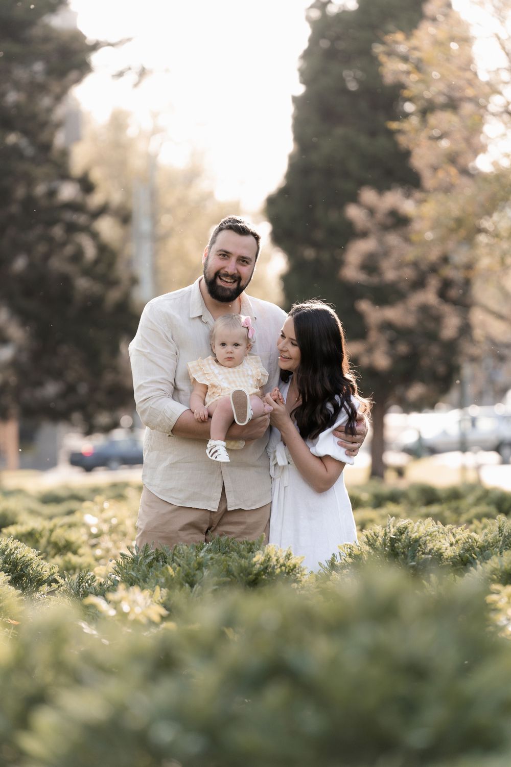 Young family shares tender moment together in sunlit garden setting.