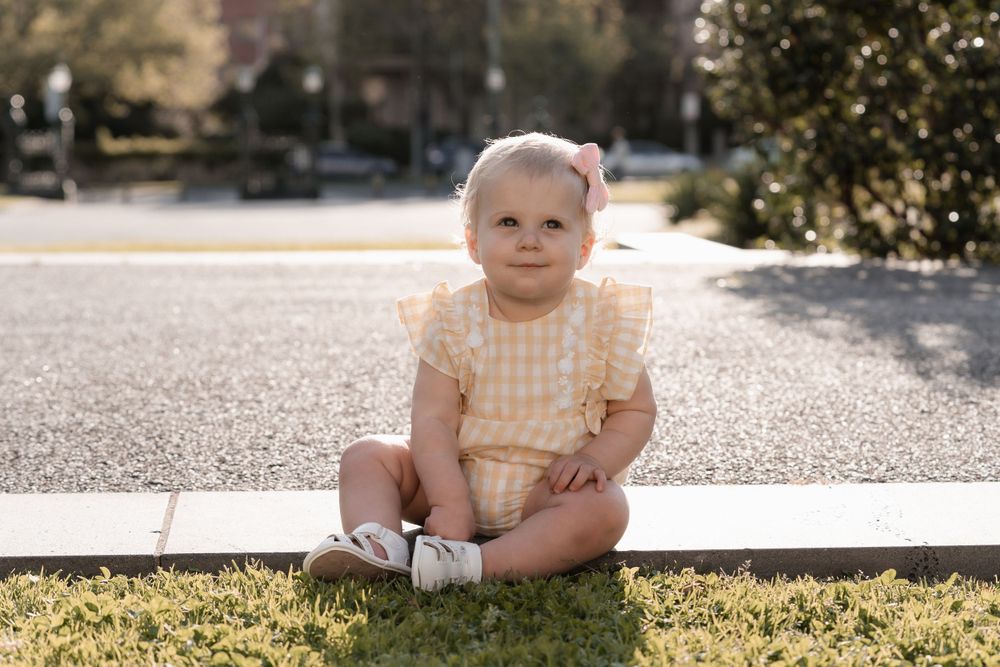 Sweet baby in yellow dress sitting on sunny outdoor patio.