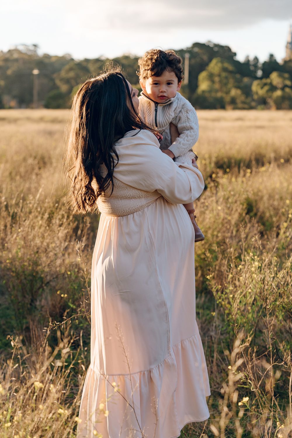 Parent and child sharing embrace in golden sunlit field at sunset.