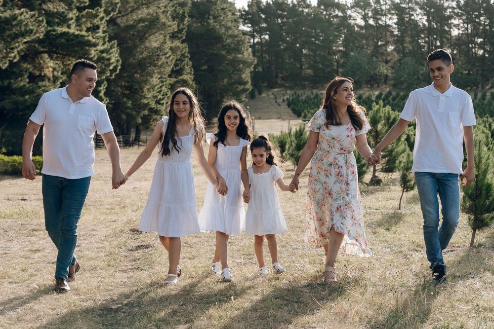Family group walking together through scenic wooded area in coordinated white outfits.