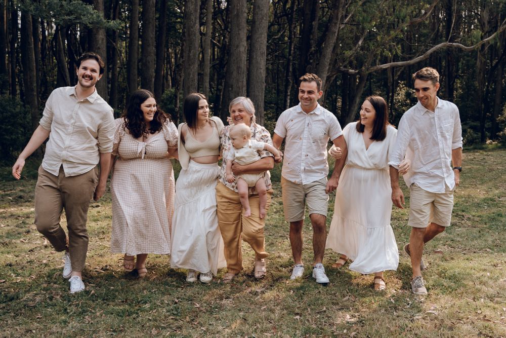 Wedding party in neutral colors walking together and smiling on grassy path with trees.