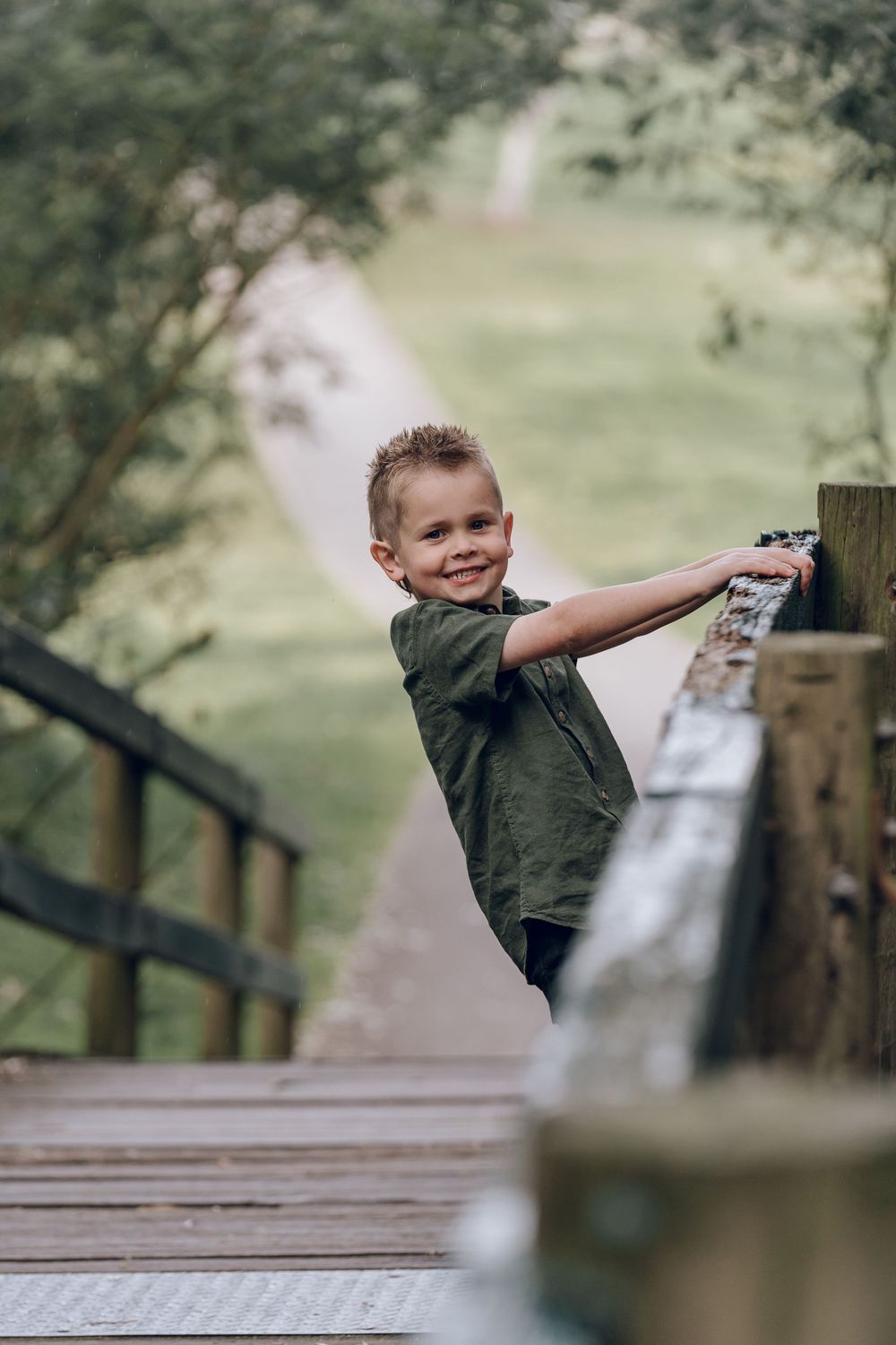 Child enjoying playful moment on wooden bridge in park setting.