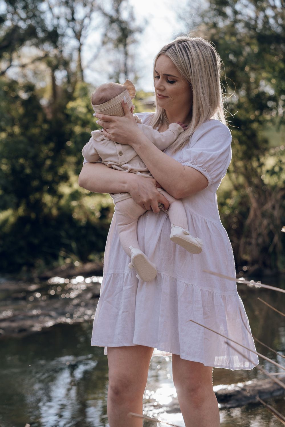 Two people in white dresses playing near riverbank on sunny day.