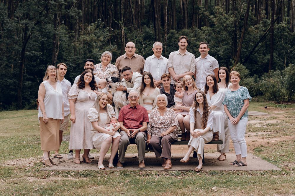Large family group portrait with multiple generations seated and standing together outdoors.