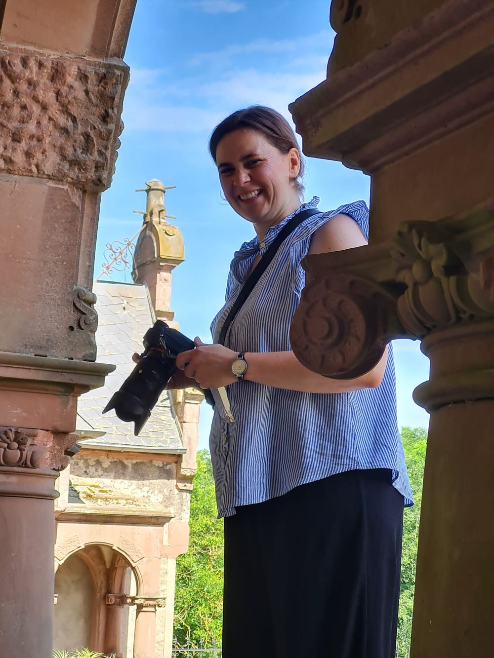 Die Fotografin Hey Elli lacht in die Kamera und steht dabei auf der Veltheimsburg ei Magdeburg, der Himmel ist blau und die Sonne scheint.