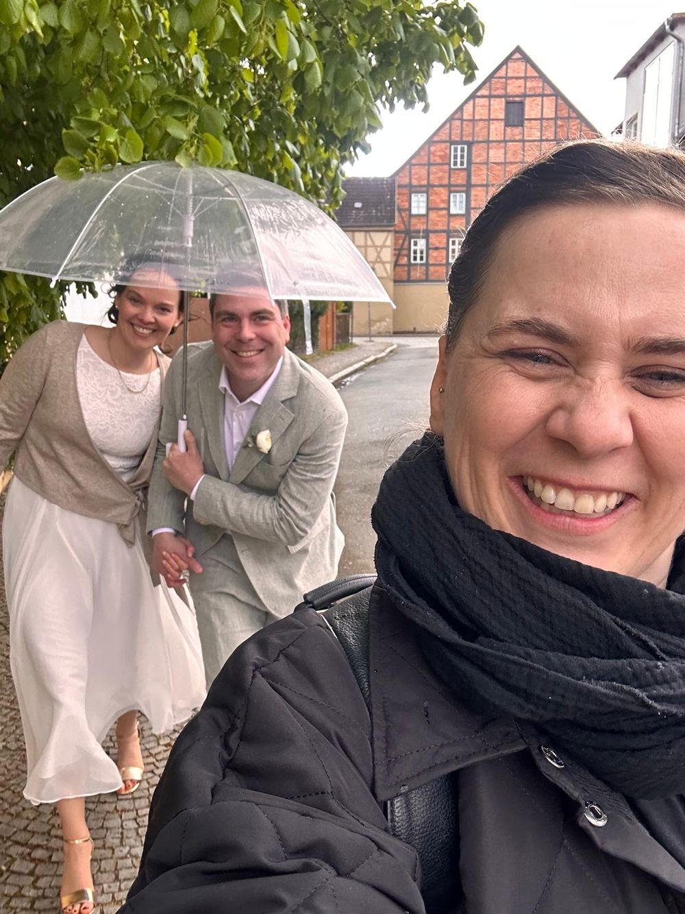Die Fotografin Hey Elli macht ein Selfie mit dem Brautpaar unter dem Regenschirm bei Regen in Quedlinburg.