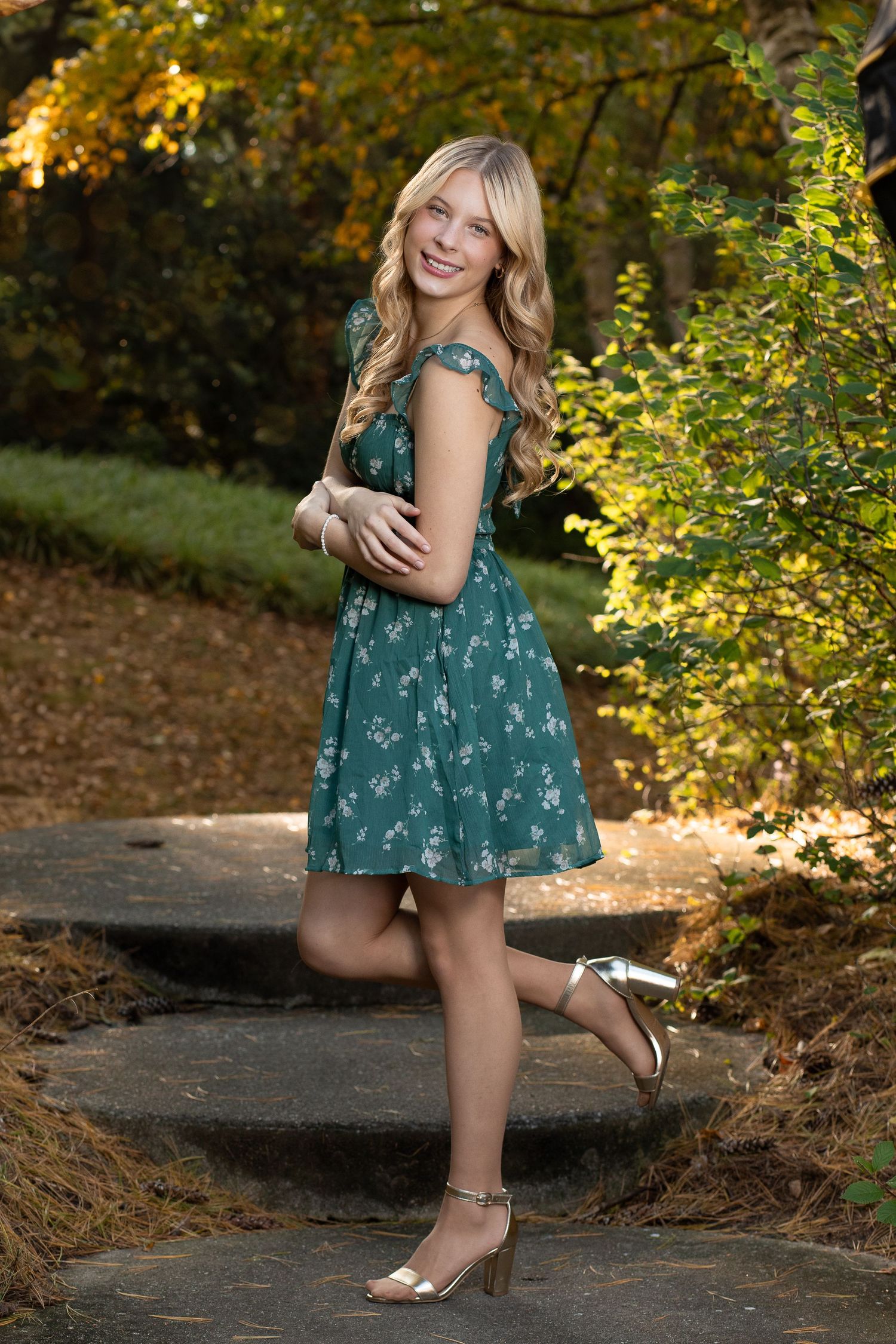 Young woman in floral green dress poses playfully on stone steps surrounded by autumn foliage.