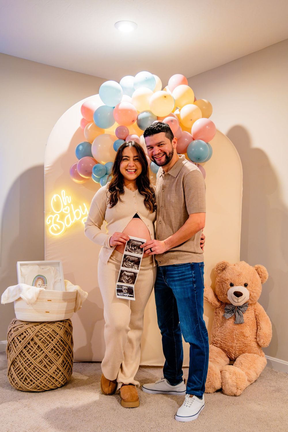 A pregnancy announcement photo series with pastel balloons, teddy bear, and ultrasound images against a neutral wall.