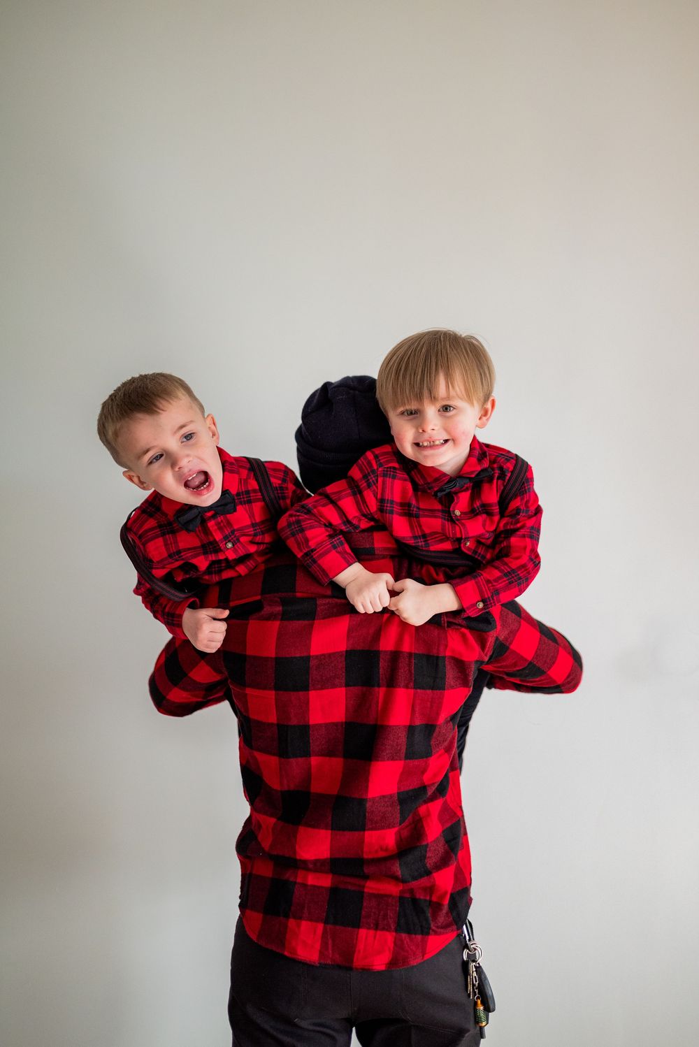 Two children in matching red buffalo plaid shirts making silly faces and poses against a white wall.