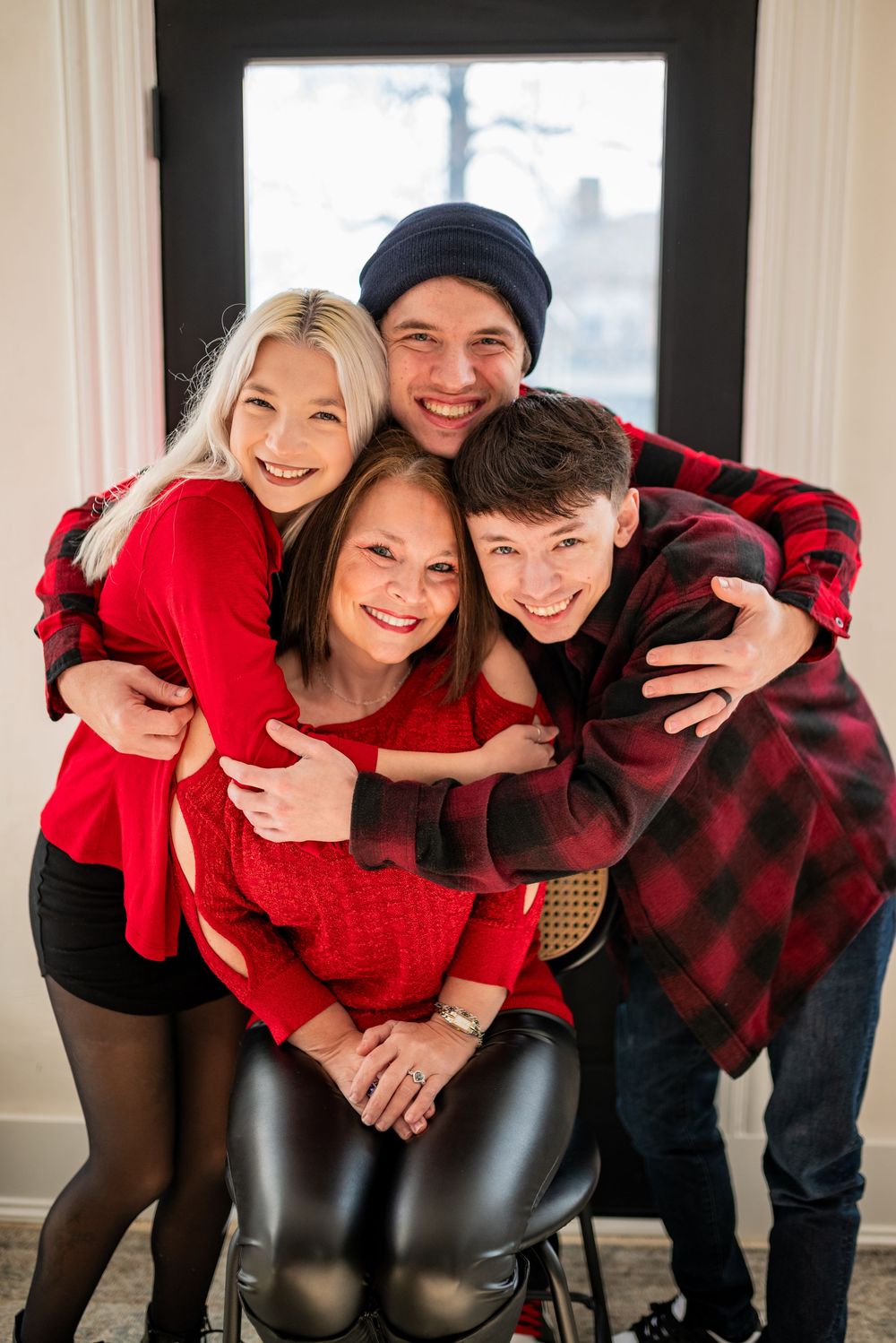 A family wearing coordinating red and black buffalo plaid outfits poses playfully together indoors.