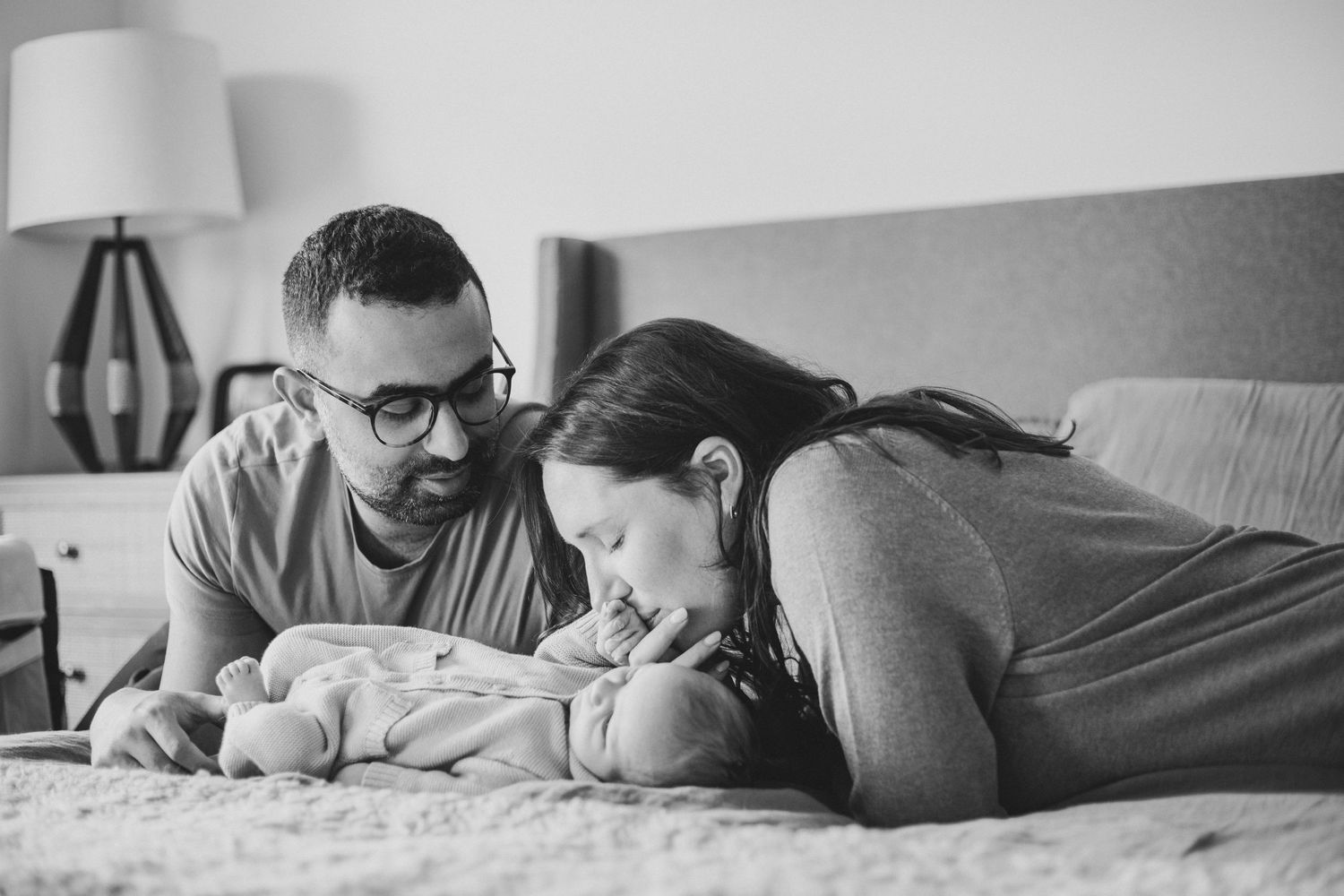A tender black and white photograph of parents bonding with their newborn baby on a bed.