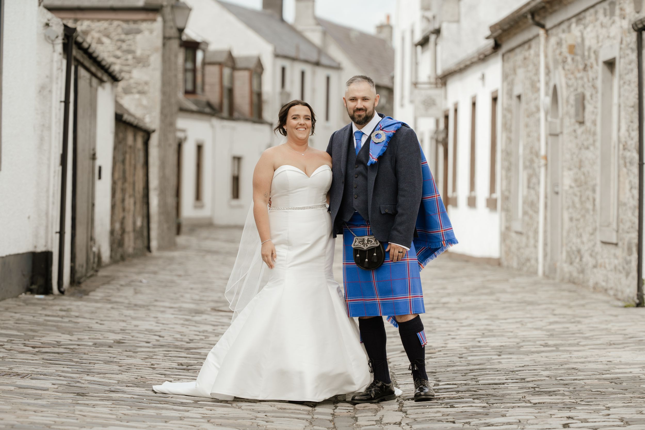 Couple in wedding attire walking through charming cobblestone streets of an old European town.