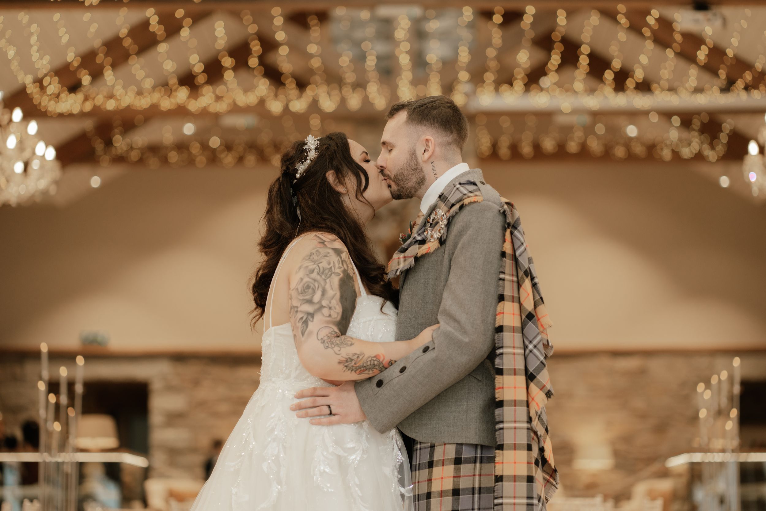 A couple shares an intimate moment during their wedding reception under warm ballroom lighting and string lights.