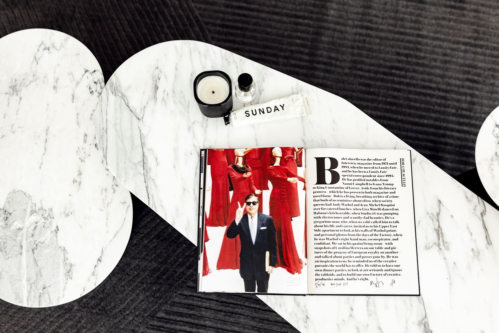 A Sunday magazine open on a marble coffee table beside a black candle.