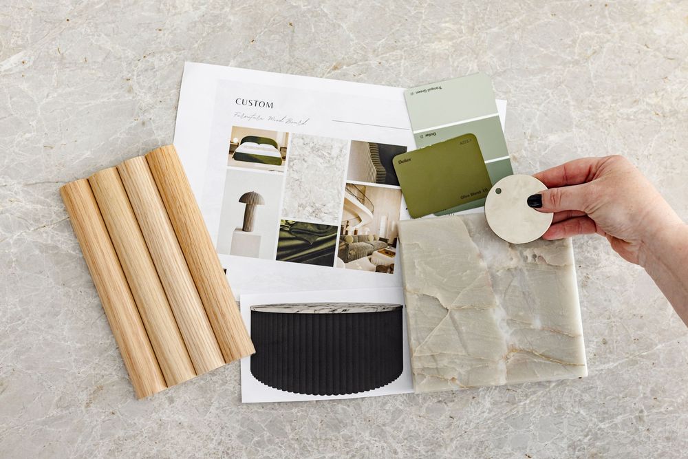A hand holding green paint swatches over an interior design mood board with wood dowels.