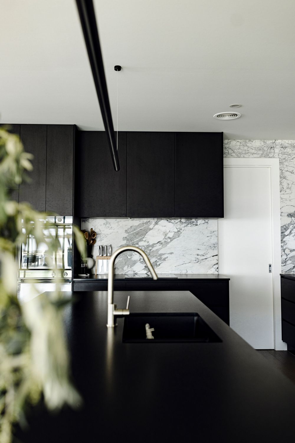 Modern black kitchen with marble backsplash, dark cabinetry, and gold faucet.
