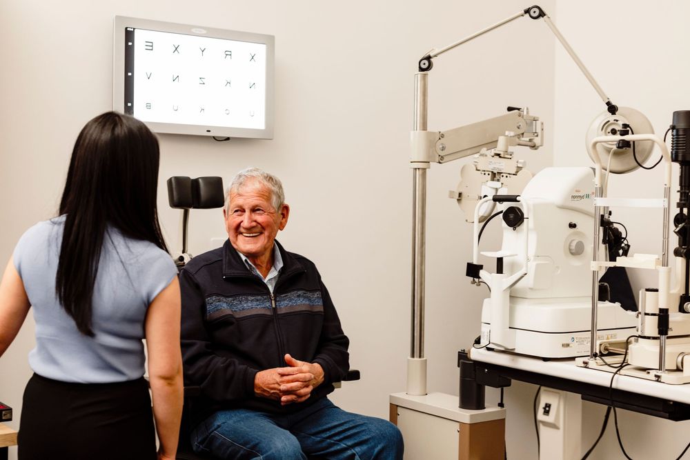 Elderly male patient smiling during an eye examination with an optometrist.