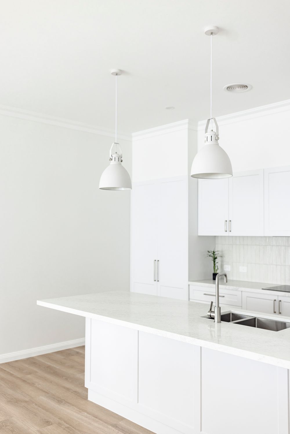 Modern all-white kitchen with pendant lights, marble countertop island, and subway tile backsplash.
