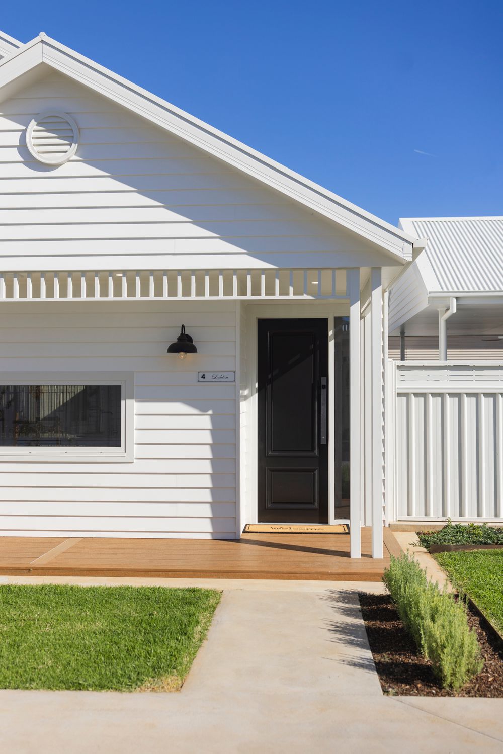 Charming white weatherboard home exterior with black front door, timber deck, and manicured lawn.