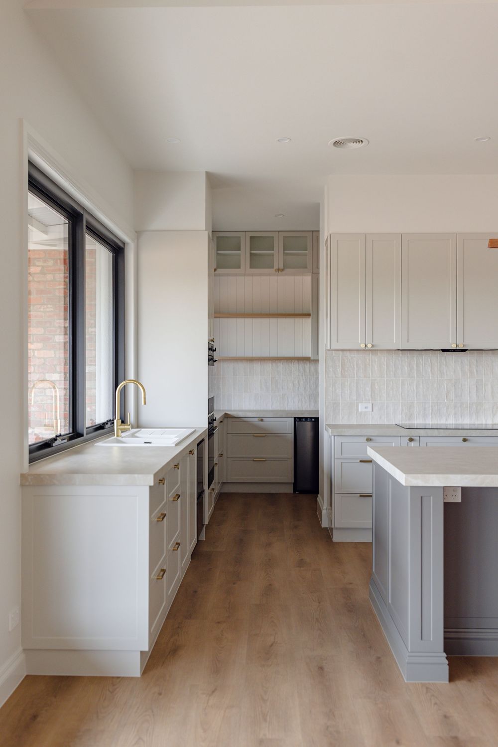 Elegant white kitchen with shaker cabinets, brass fixtures, island bench and light timber floors.