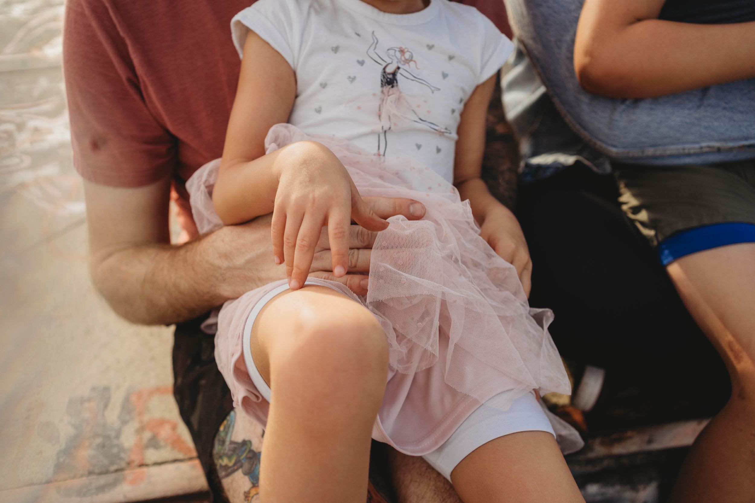 Close-up view of hands resting on a pink tulle dress outdoors.