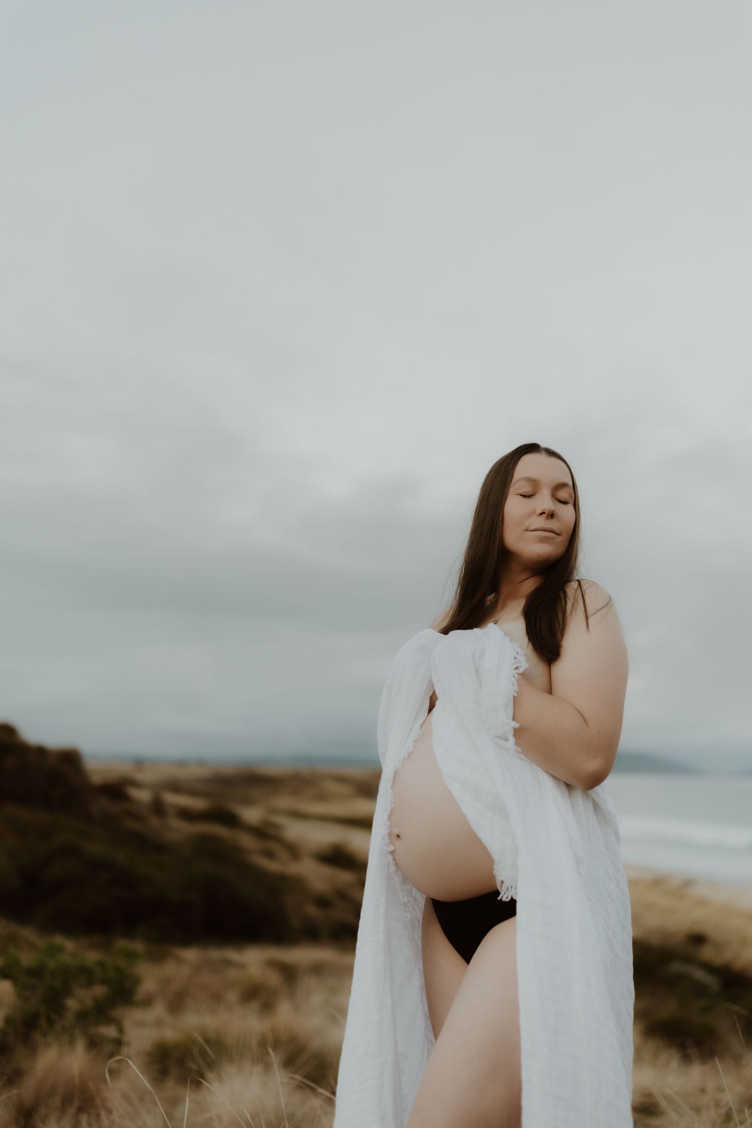 Artistic maternity silhouette against moody coastal landscape.