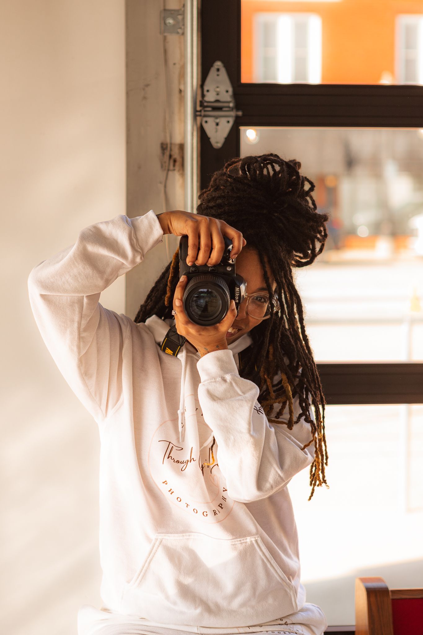 Person in white hoodie taking photos with professional camera.