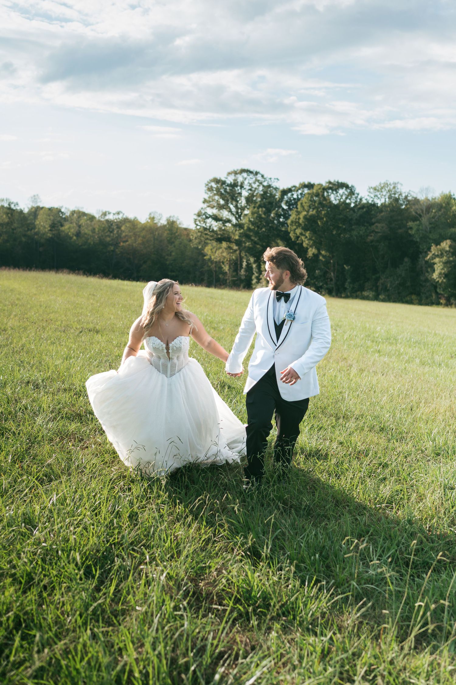 Bride and groom posing in white gown and gray suit on green field with stormy sky High Point NC