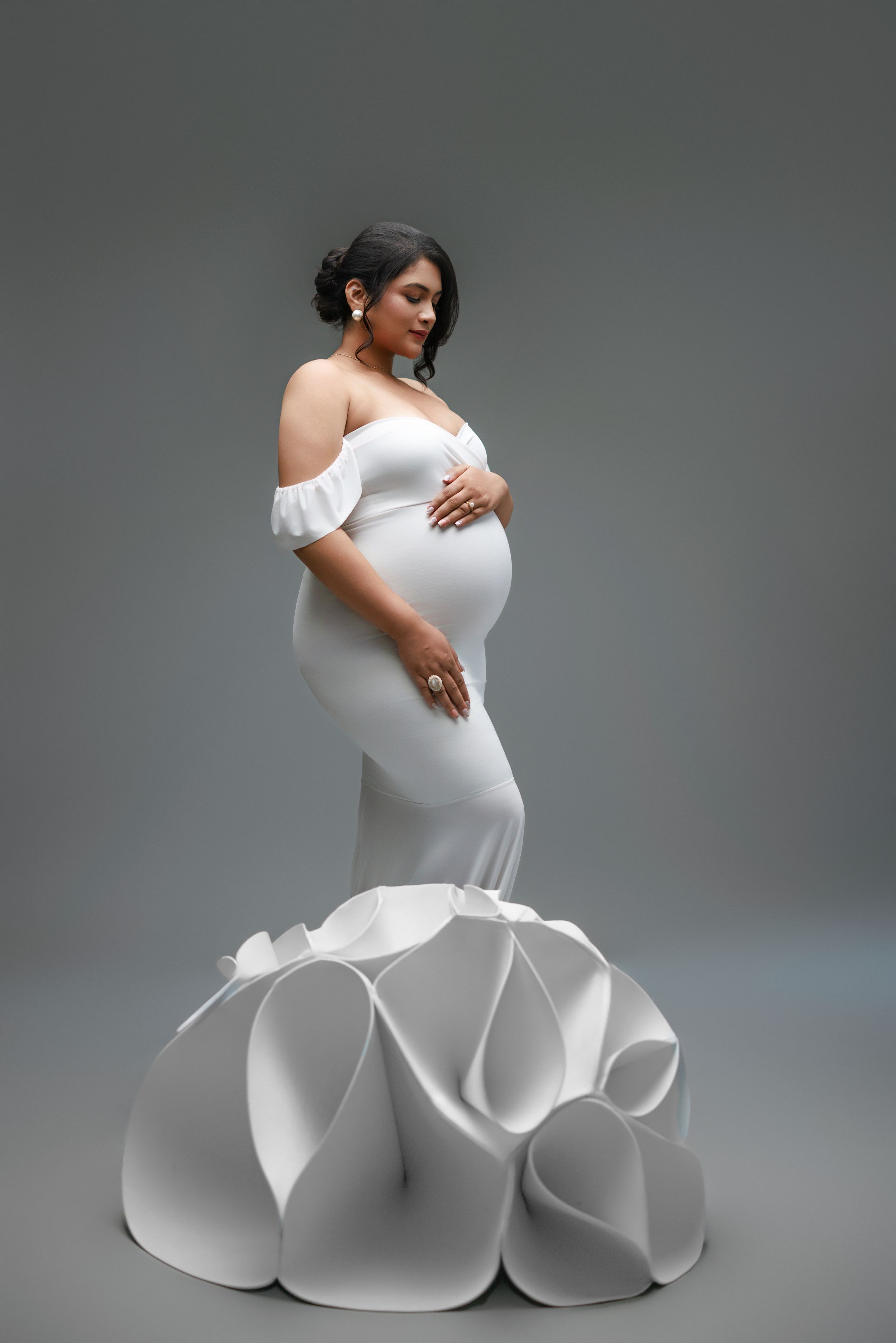 Elegant maternity photo featuring a white off-shoulder mermaid gown with dramatic sculptural ruffles at the bottom.
