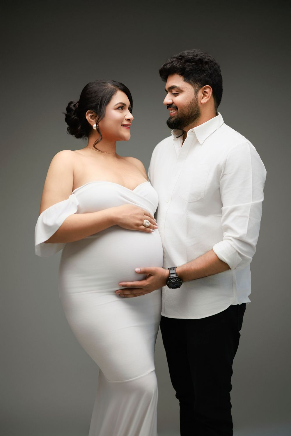 A series of maternity photos showing intimate moments between expectant parents in white and black outfits against a grey backdrop.