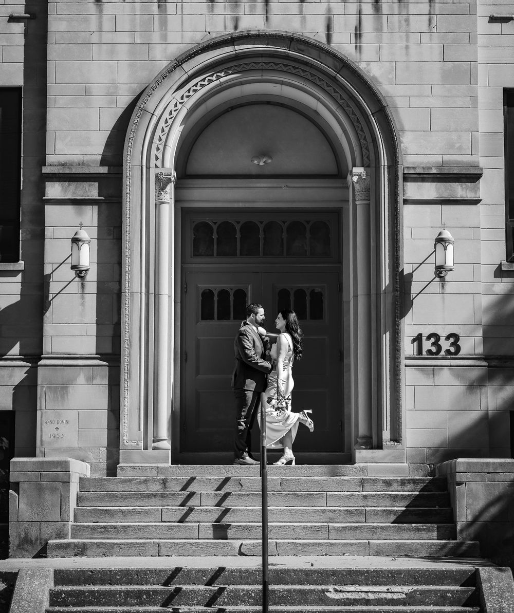 Couple embracing in a grand archway entrance of a historic stone building with the number 133.