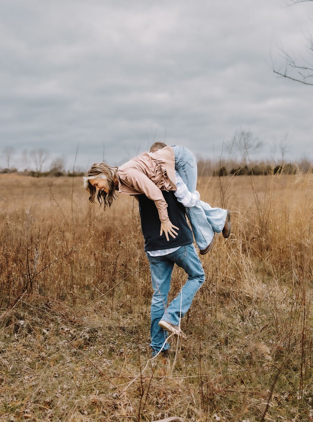 A playful couple having fun in a rustic field under moody skies.