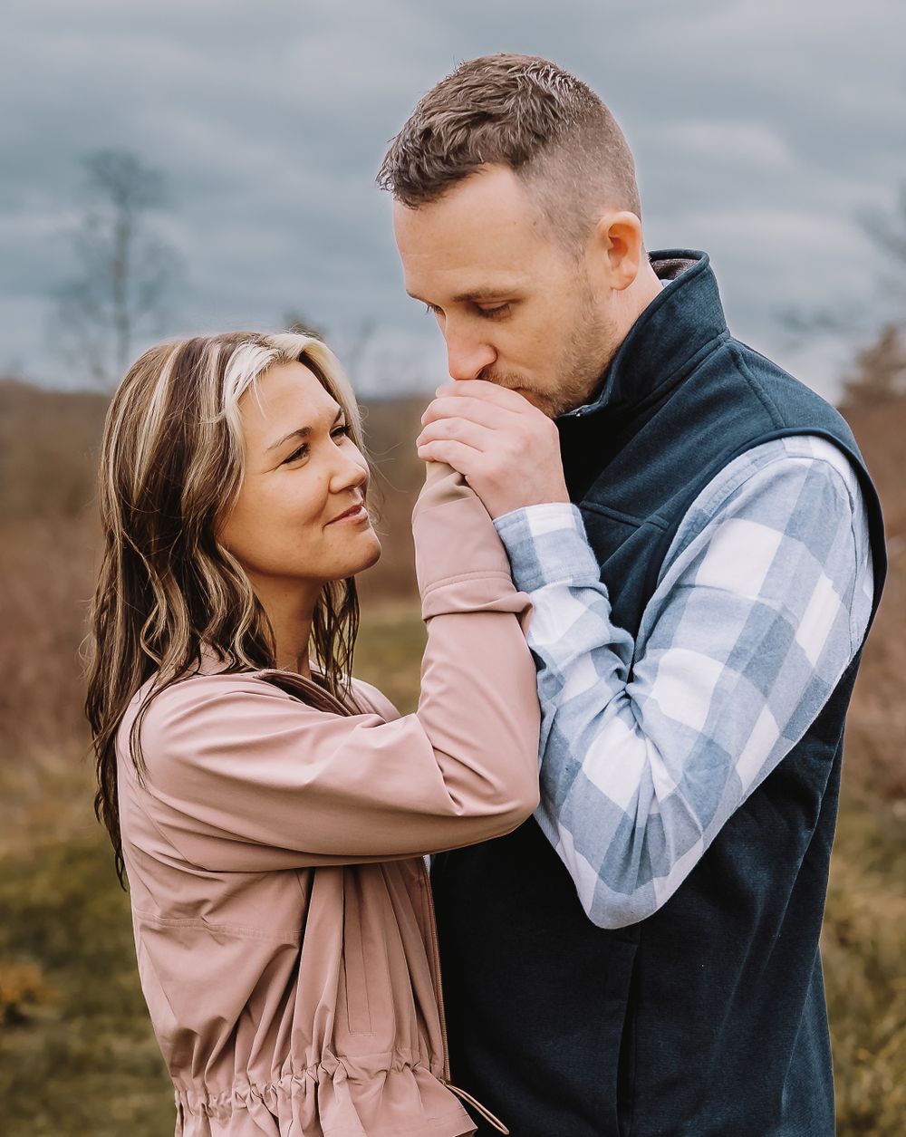 A couple shares a tender moment outdoors in a romantic engagement photo sequence wearing pink and plaid.