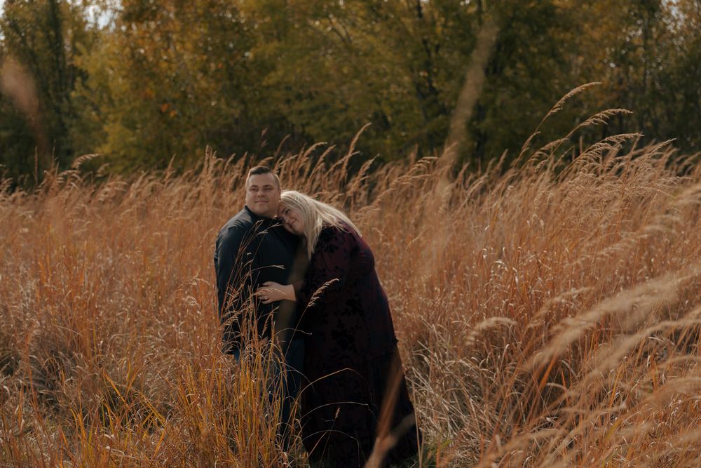 A couple walks through tall golden grass in a field during autumn with sunlight creating a warm atmospheric glow.