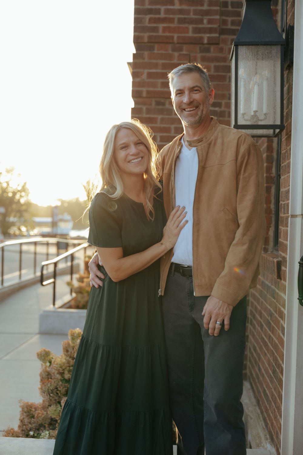 A couple shares a romantic moment together outside a brick building during golden hour sunset.