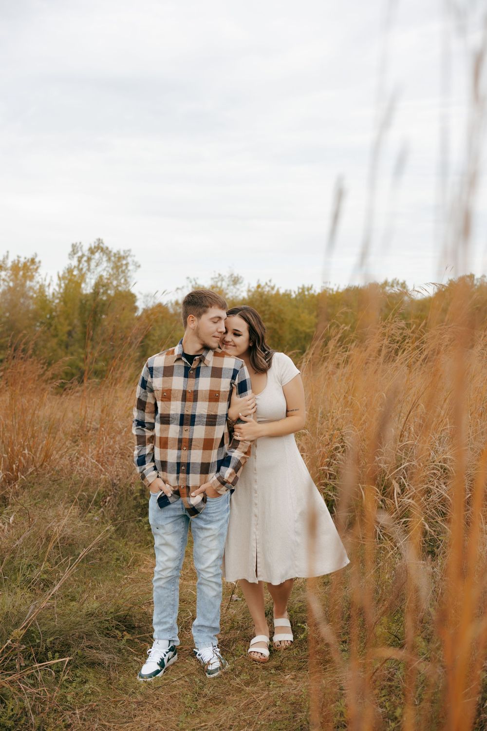 A couple embraces in a romantic autumn field with tall golden grass and warm sunlight.