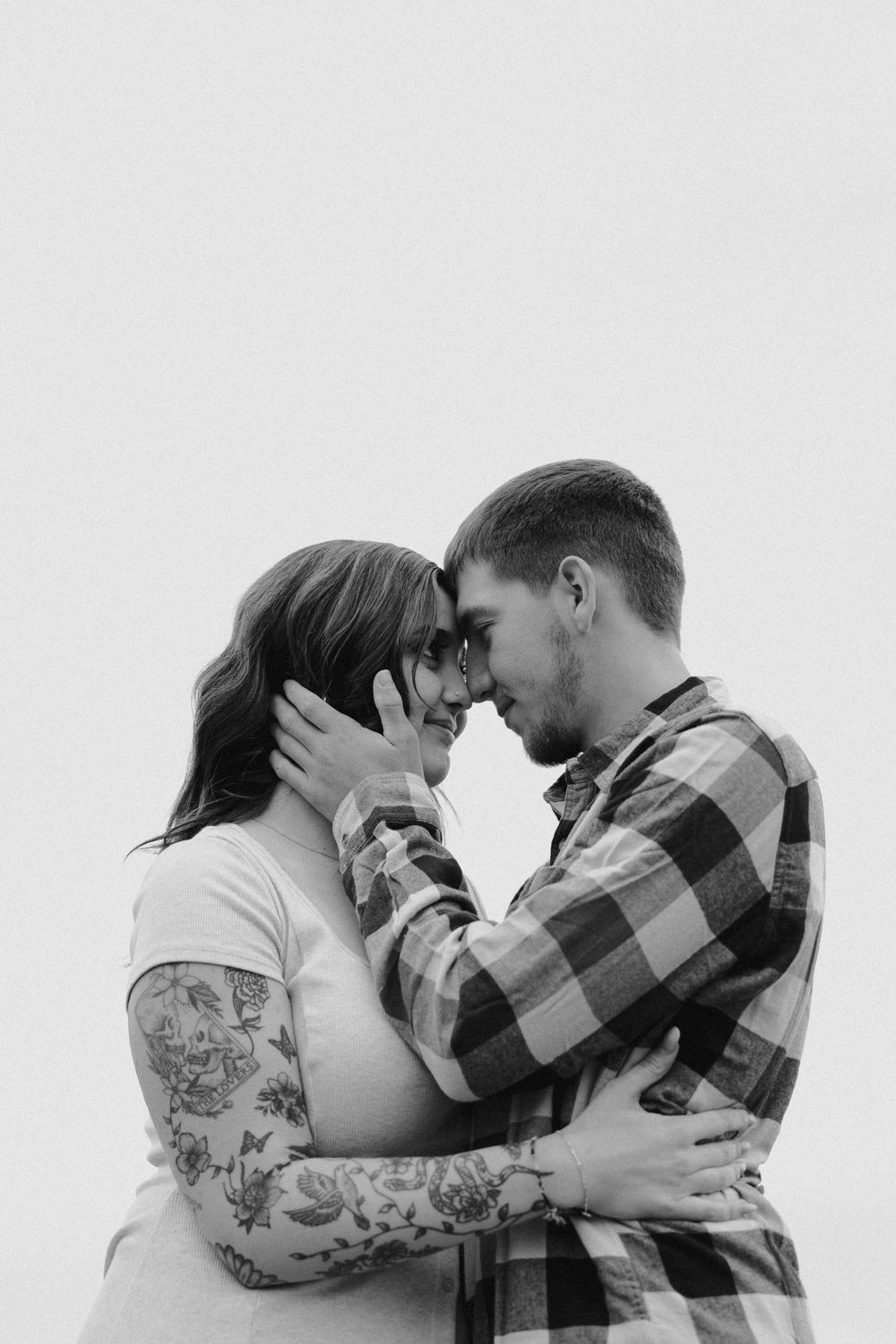 A couple shares a tender kiss while embracing in black and white, with one person wearing a plaid shirt.