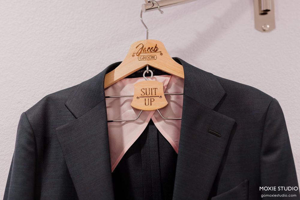 A row of dark gray and black suit jackets hanging on wooden hangers against a white wall.