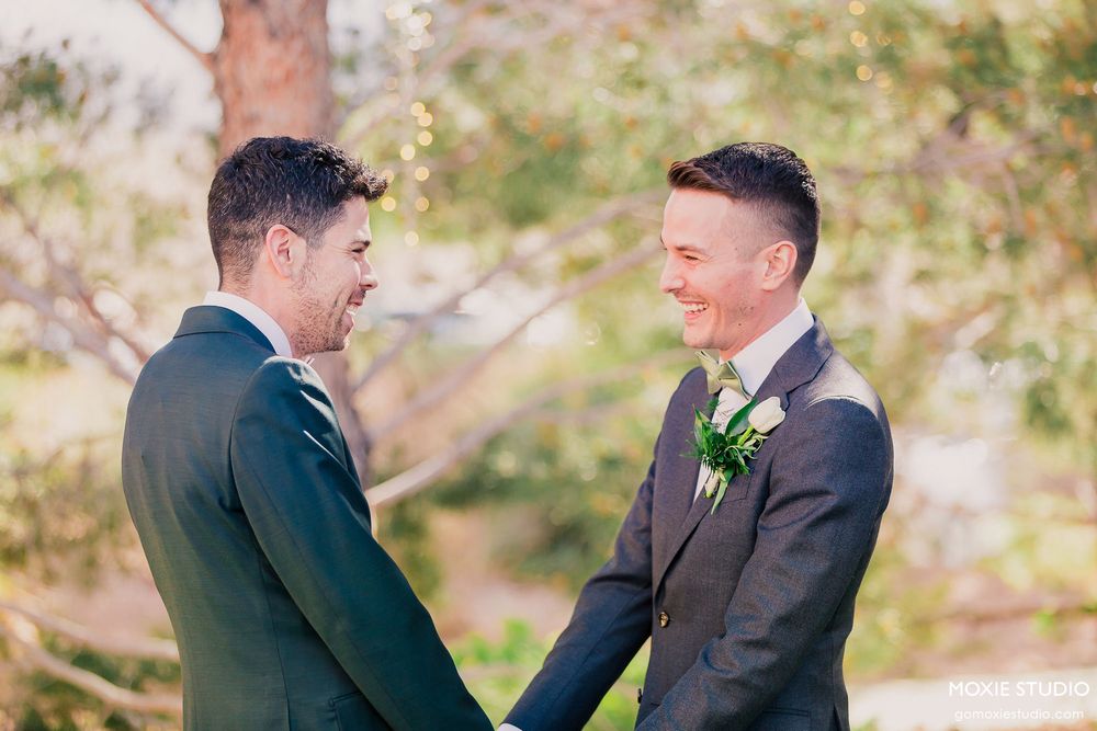 Wedding party members interact and laugh together outdoors in formal attire.