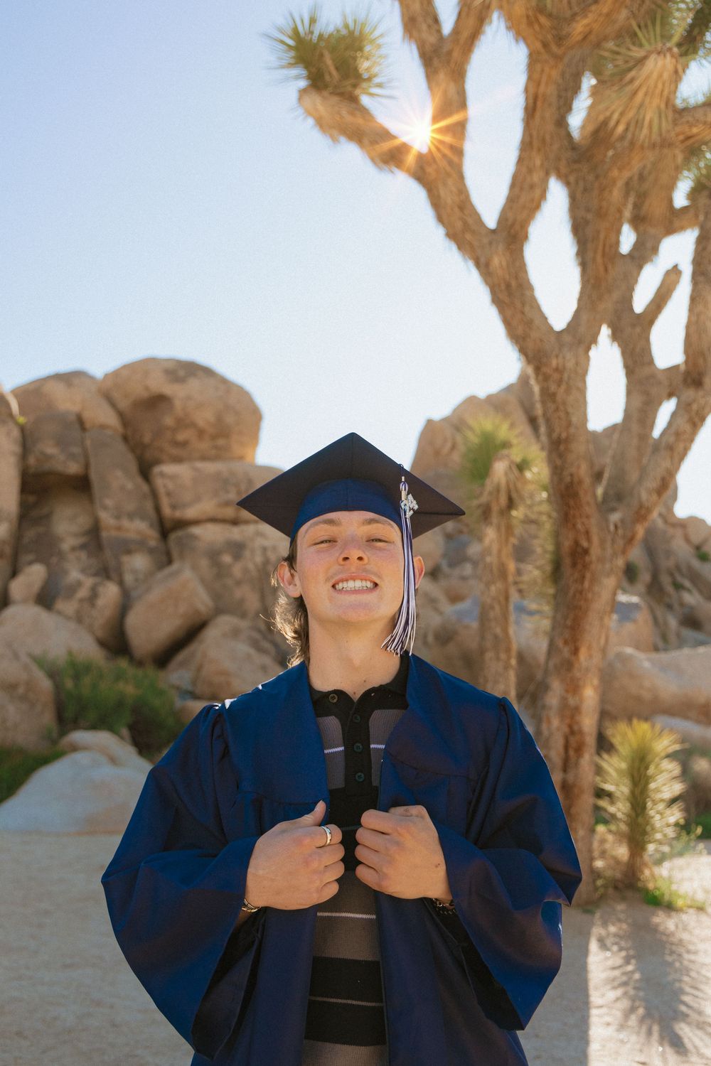 Graduate celebrates in desert landscape with joshua trees and rock formations in the background.